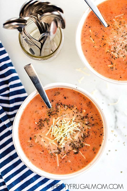 crockpot tomato basil soup in two white bowls with spoons next to dish towel