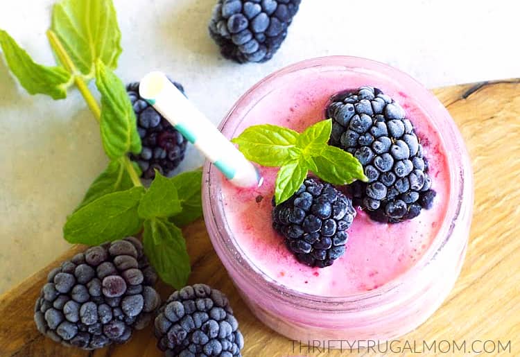 glass of yogurt and frozen fruit smoothie with frozen blackberries and sprigs of mint