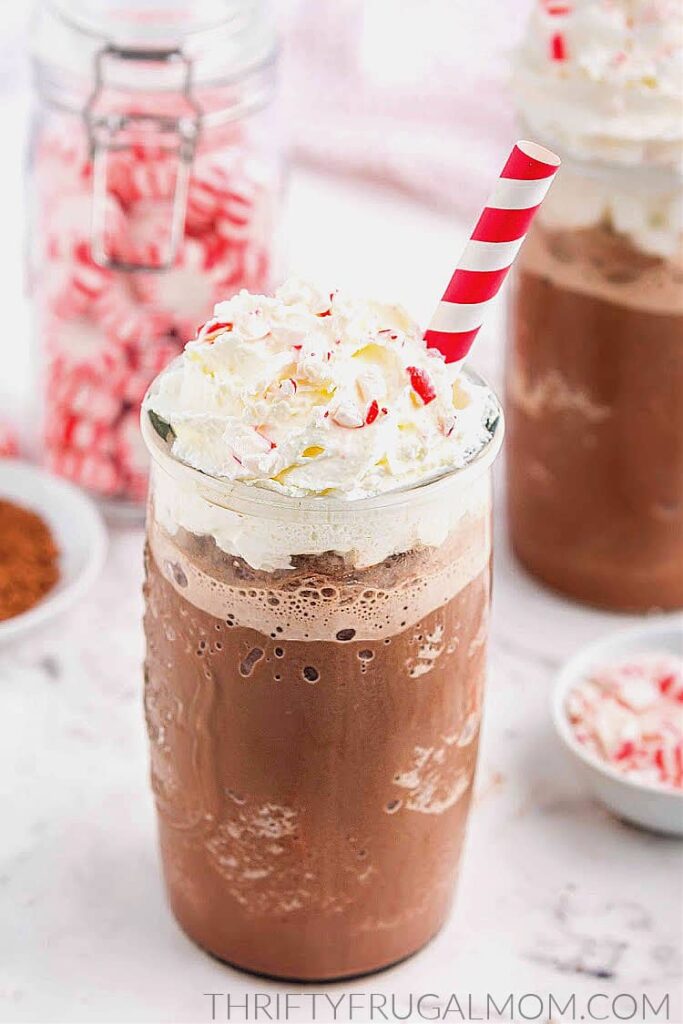 a glass of Starbucks copycat peppermint mocha frappuccino with whipped cream on top and a white and red straw with peppermint candy in background
