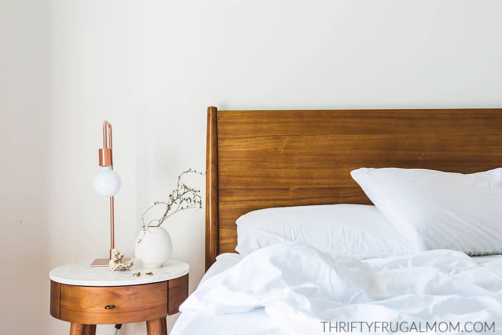a wooden bed and nightstand with a white bedspread and pillows