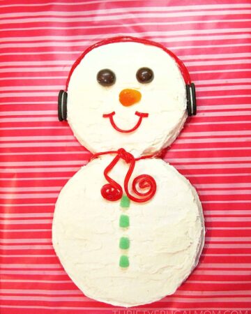 a simple homemade snowman cake made from round cakes on a pink striped background