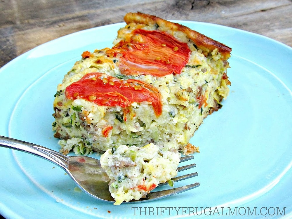 piece of baked hamburger zucchini quiche topped with sliced tomatoes on a blue plate