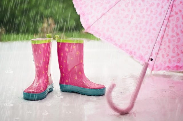 pink and yellow rain boots next to a pink umbrella with rain pouring down
