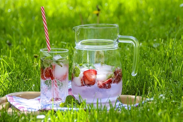 A glass and pitcher of water with strawberries sitting on the grass