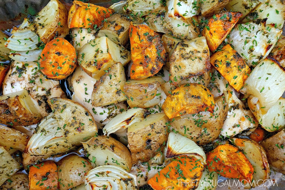 close up of herb roasted chicken, potatoes, sweet potatoes and onions in baking dish