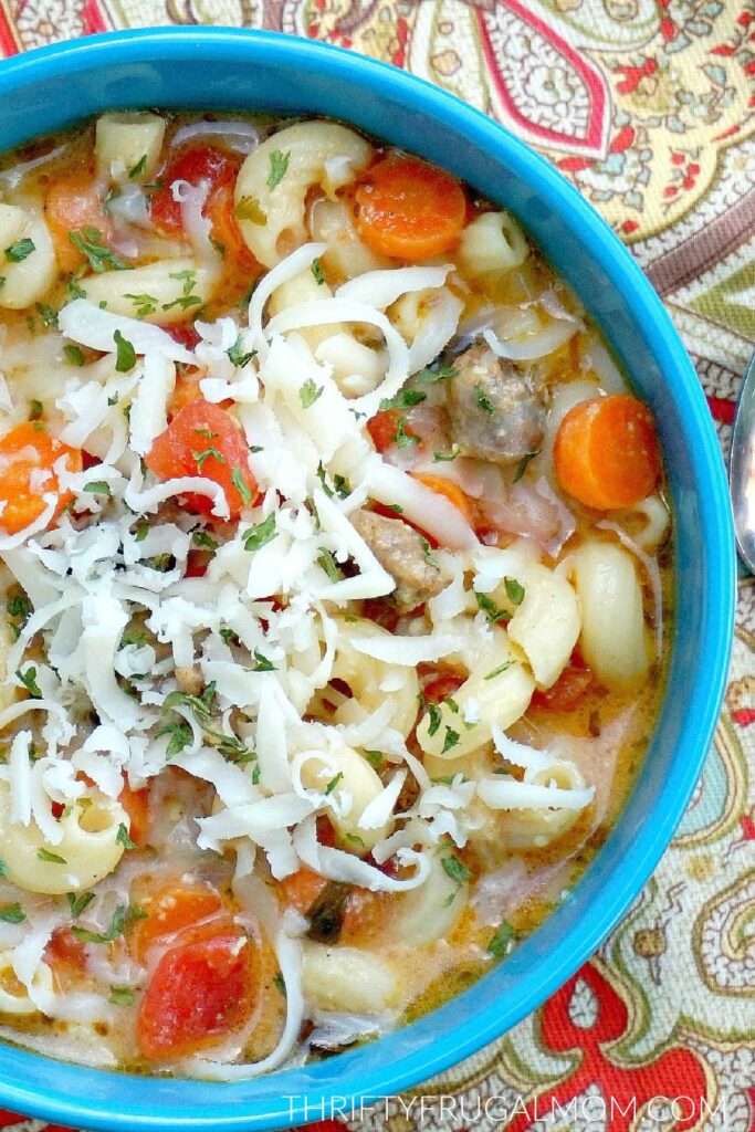 a closeup of a bowlful of Italian Sausage and Pasta soup topped with shredded mozzarella cheese