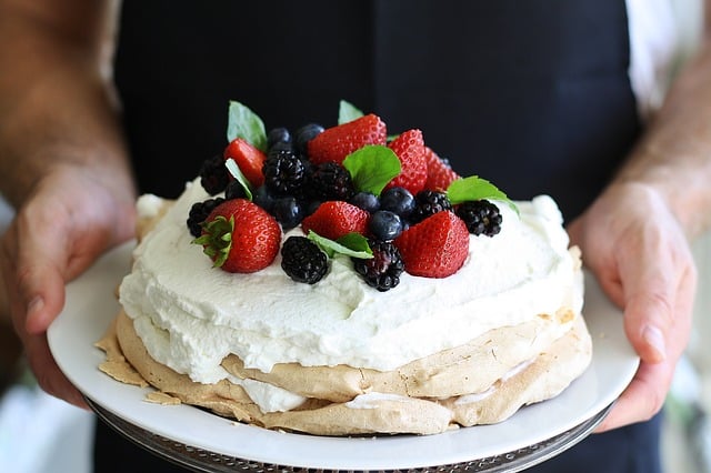 two hands holding a white plate with a dessert topped with fresh berries