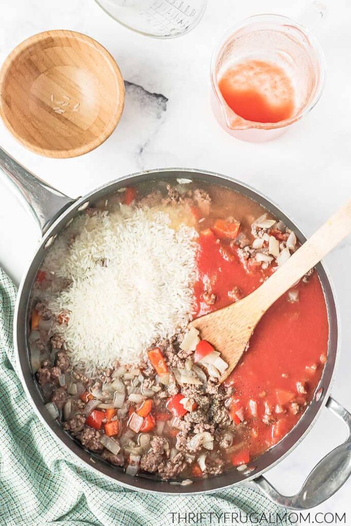 seasonings, rice, water, and tomato juice added into the skillet with a wooden spoon