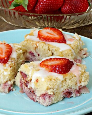 a plate with 3 slices of Fresh Strawberry Yogurt Cake topped with lemon glaze and sliced fresh strawberries