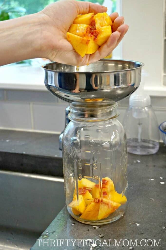 peaches being pour into a funnel topped canning jar