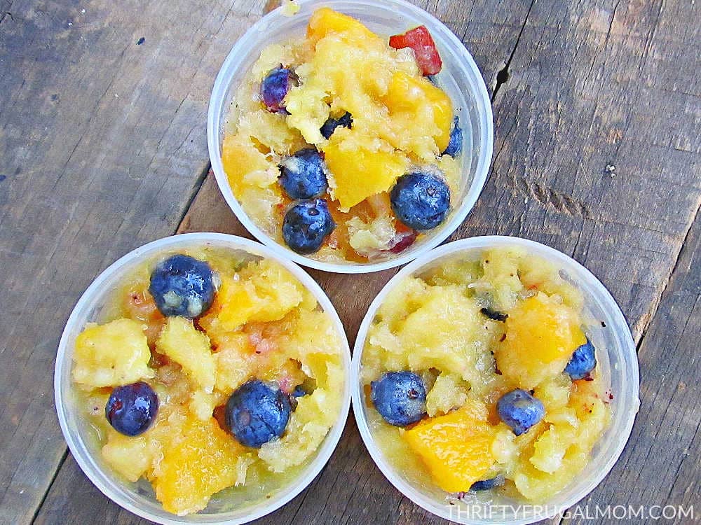 Three frozen fruit cups with grapes, blueberries, pineapple, peaches and bananas