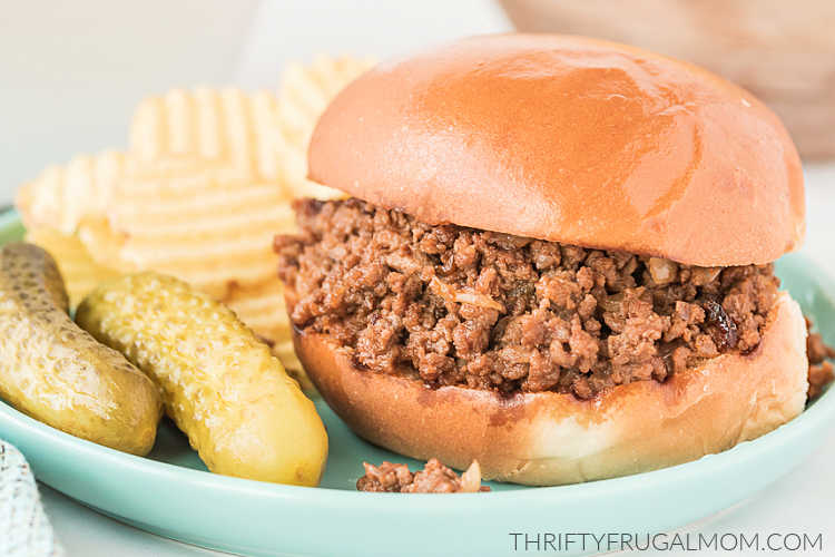 a homemade Sloppy Joe sandwich with potato chips and pickles on an aqua plate
