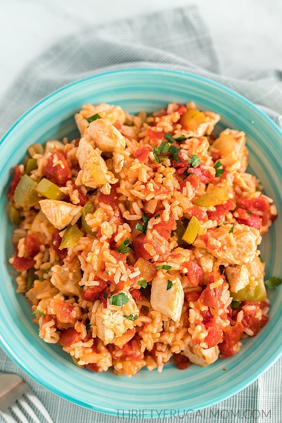 spanish chicken and rice with tomatoes and peppers in an aqua colored bowl