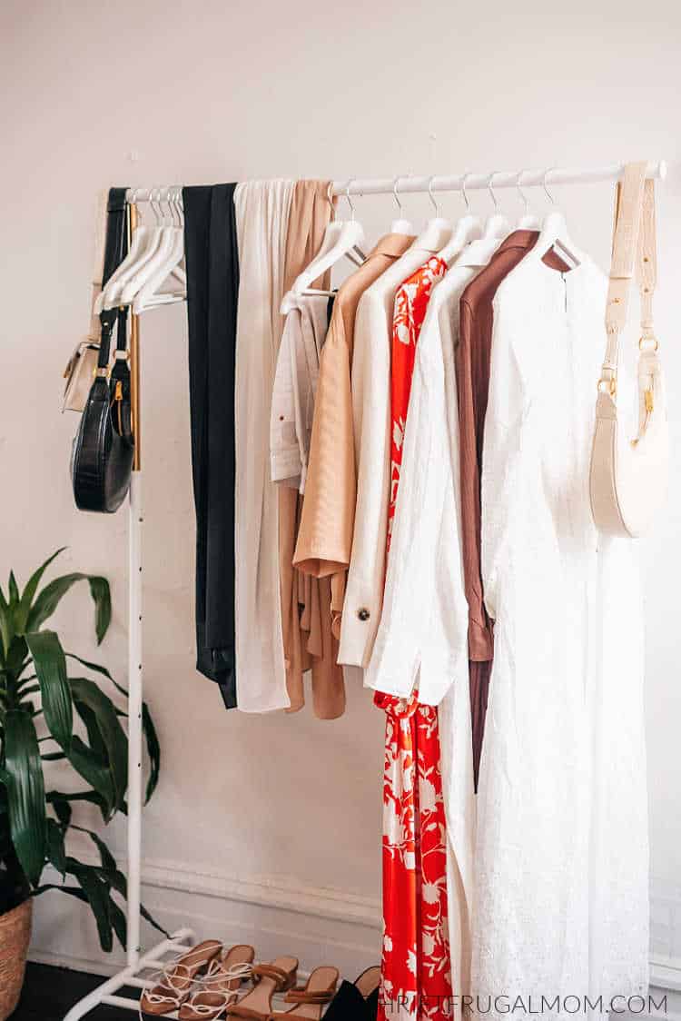 a white rack with various pieces of clothing having from it on hangers