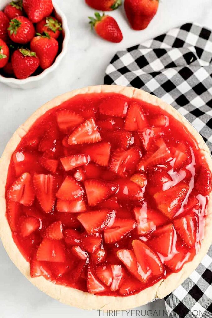 strawberry pie next to a bowl of whole strawberries and a buffalo plaid cloth