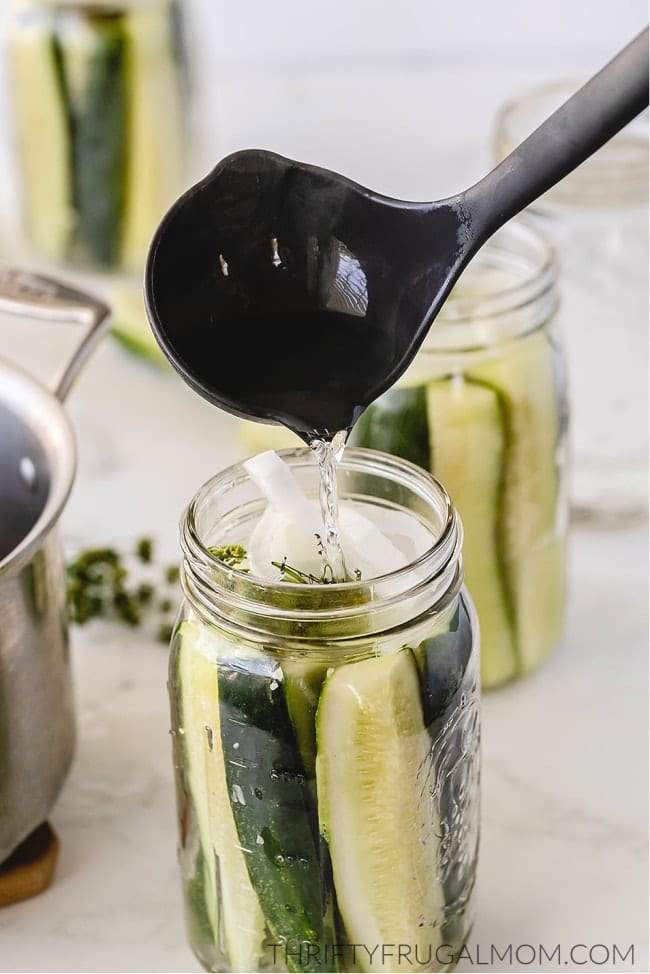 Brine being ladled into dill pickles in canning jar 