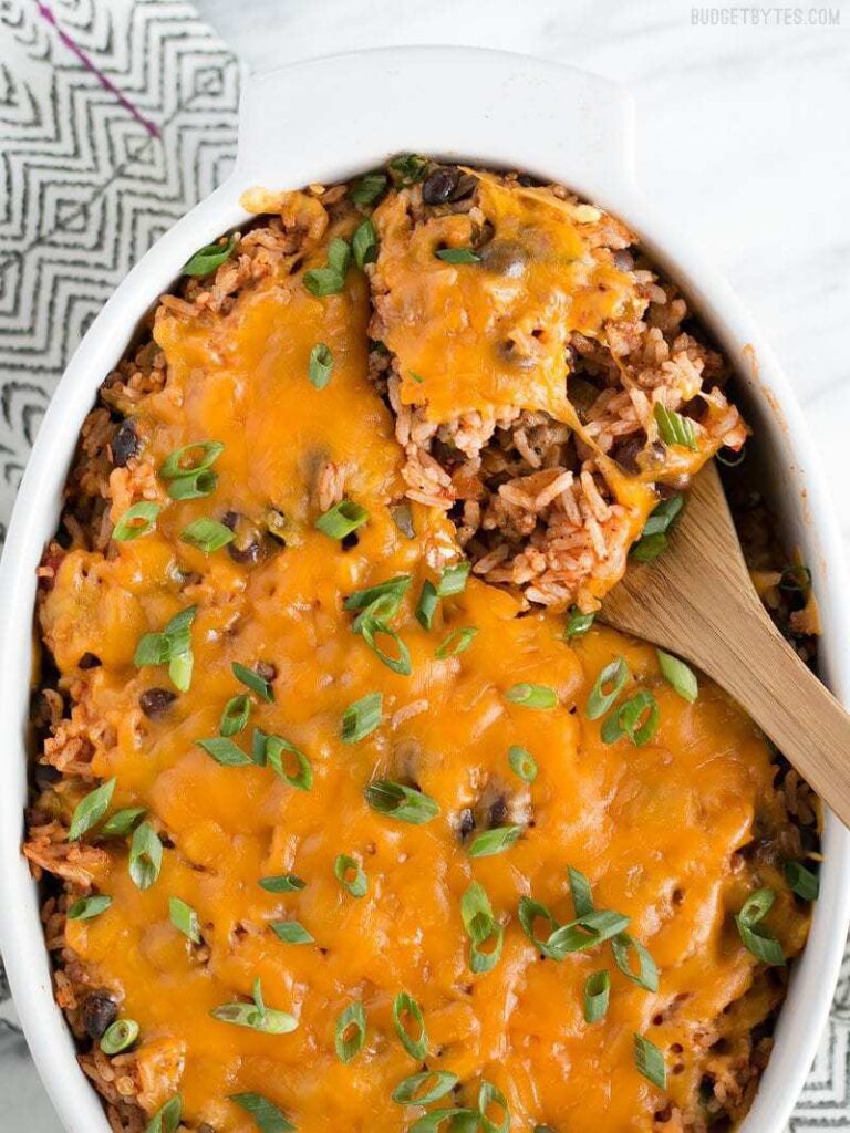 Budget friendly Beef Burrito Casserole in an oval white baking dish being spooned out with a wooden spoon