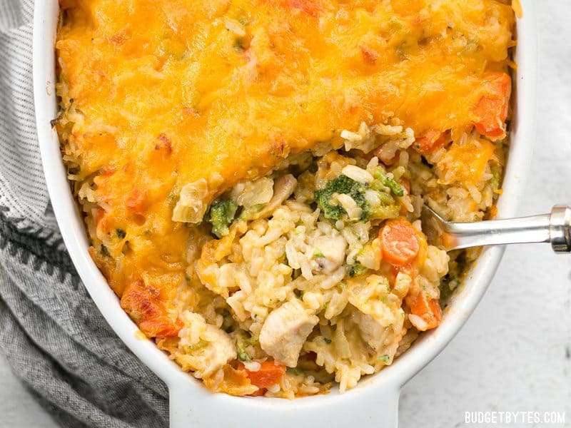 budget friendly Cheesy Chicken, Vegetables and Rice Casserole being spooned out of a white baking dish