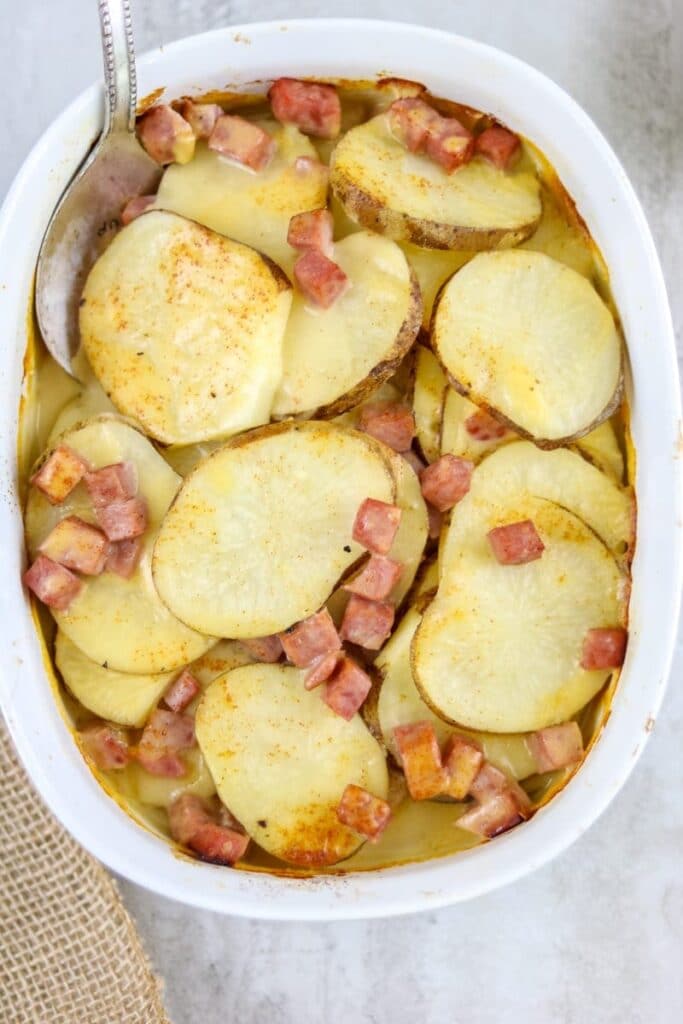An easy dinner casserole of Cheesy ham and scalloped potatoes in a white baking dish with a spoon