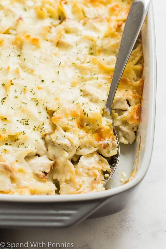 Chicken Alfredo Bake in a white casserole dish with a spoon in it- an easy cheap dinner casserole