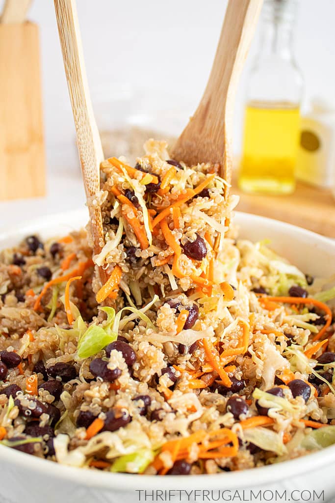 Easy Quinoa Cabbage Salad being scooped out of a white bowl using wooden tongs