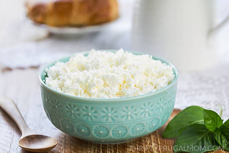an aqua bowl full of ricotta cheese on a wooden table with a spoon and fresh herbs
