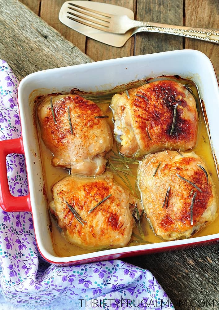 baked chicken thighs in a red baking dish on a wooden table with a lavender floral cloth beside it