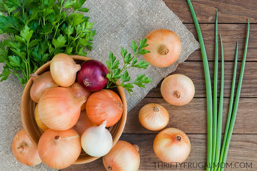 a wooden bowl full of onions with some onions and herbs scattered beside it.