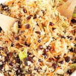 cabbage salad with quinoa and black beans in a white bowl with two wooden spoons