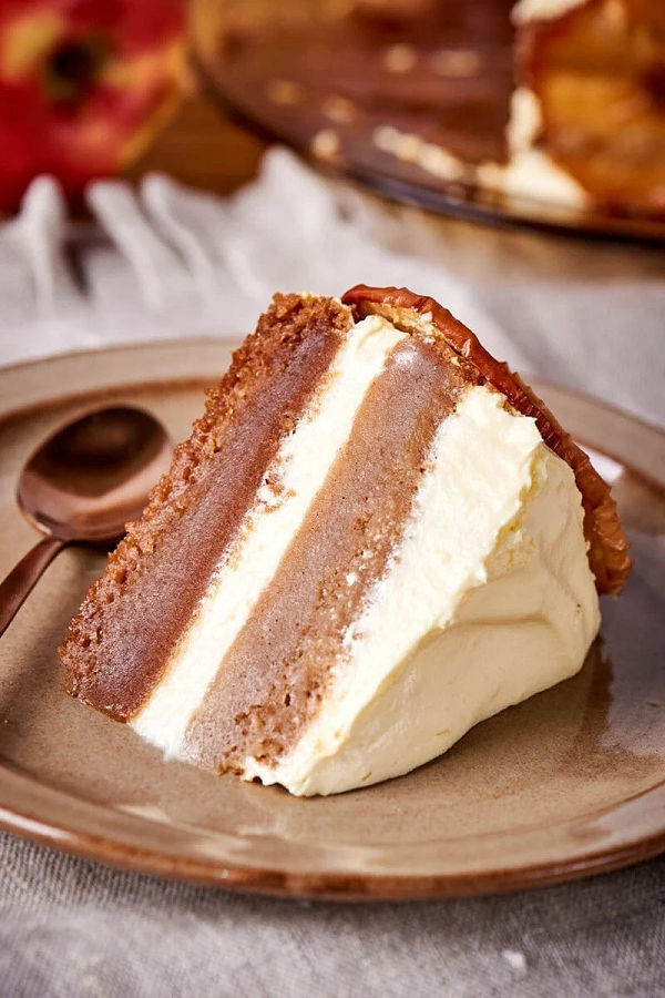 A slice of layered Applesauce Cake with Frosting laying on its side on a brown plate.