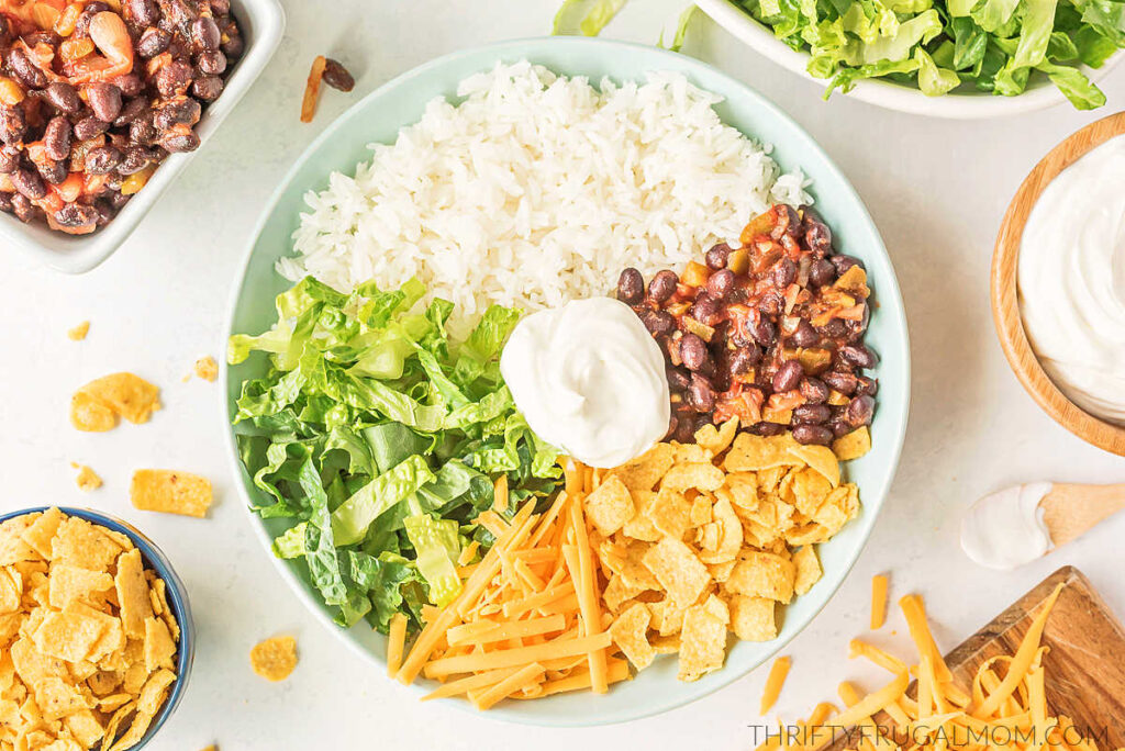 all the ingredients for a Mexican Rice Bowl assembled in a white bowl and topped with sour cream