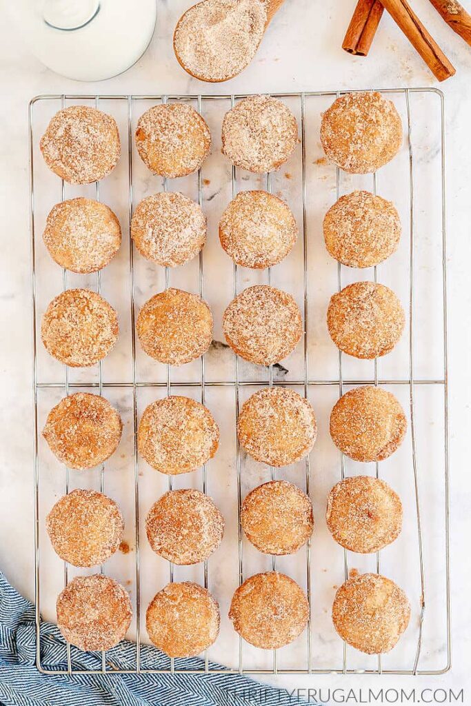 cinnamon donut muffins with a sugar coating on a cooling rack next to cinnamon sticks
