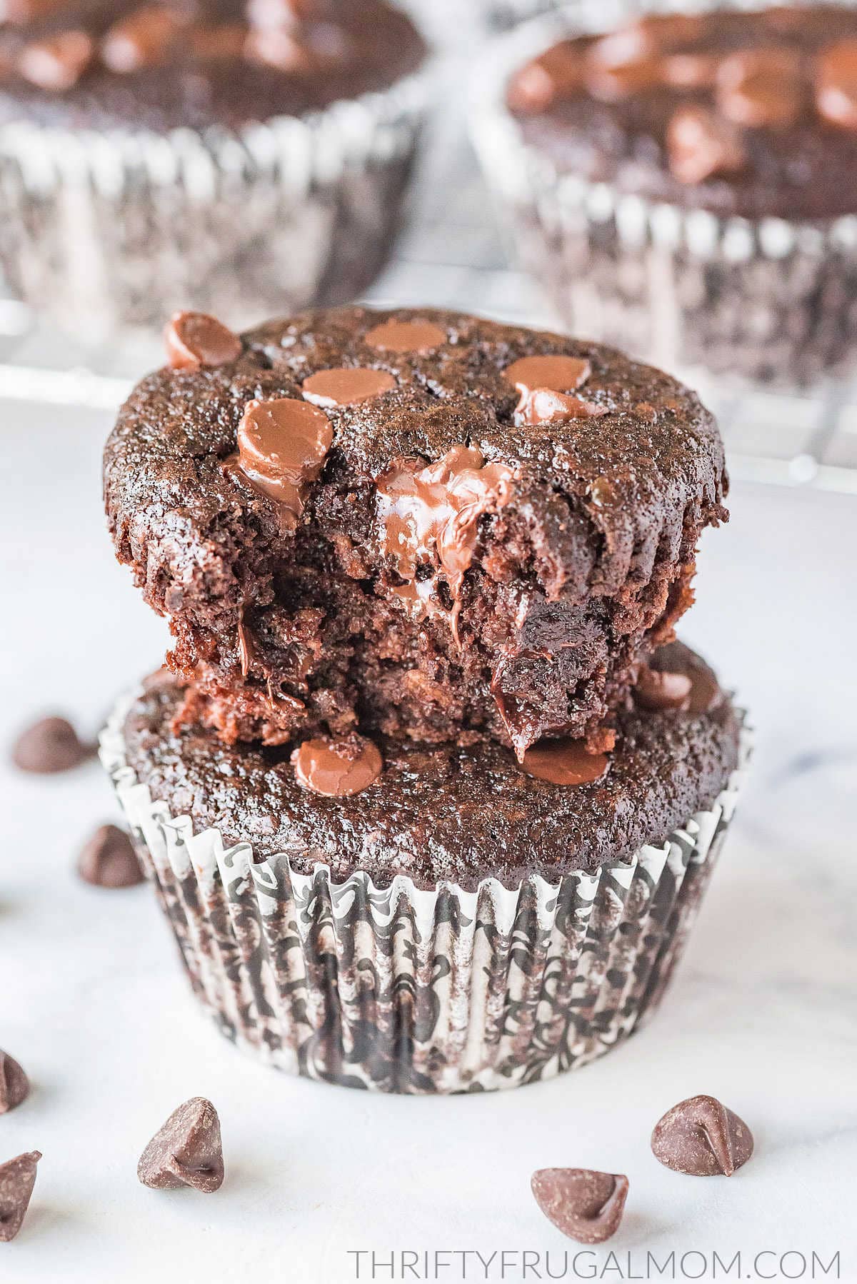 two double chocolate muffins without flour stacked on top of each other one with a bite taken out with more muffins in the background