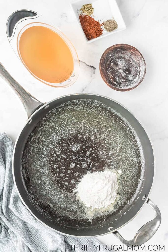 butter melted in a skillet with flour next to a cup of chicken broth and spices