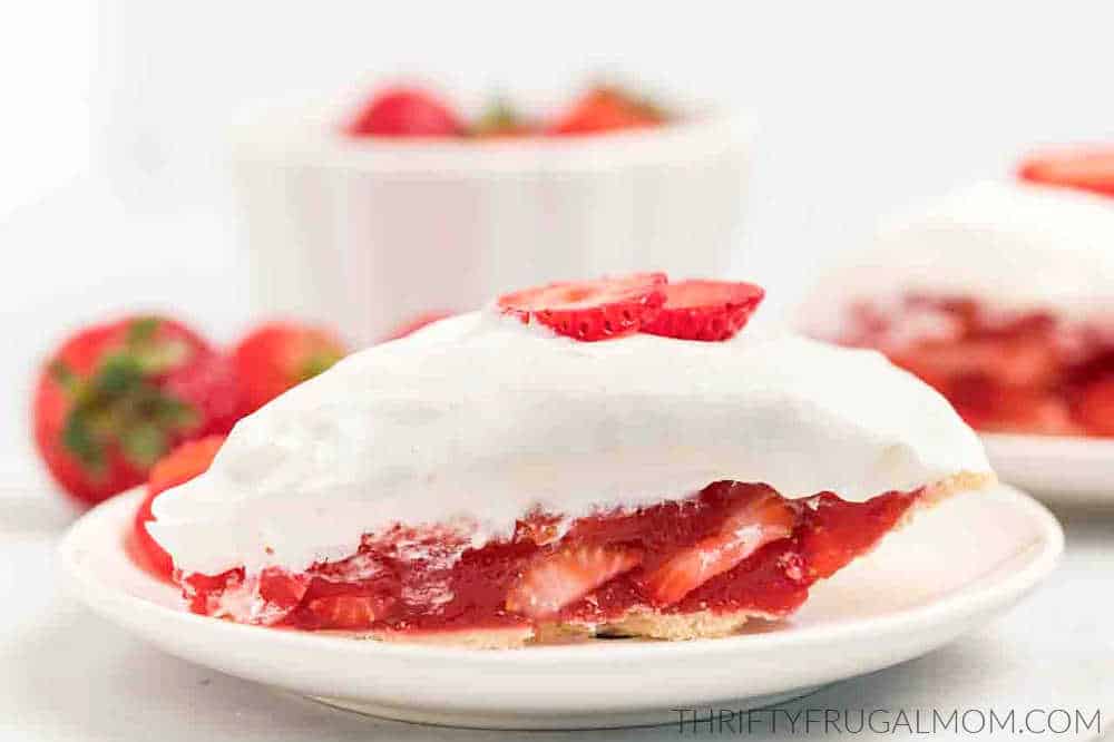 a sliced of homemade strawberry pie with jello topped with whipped cream and sliced strawberries for garnish on a small white plate