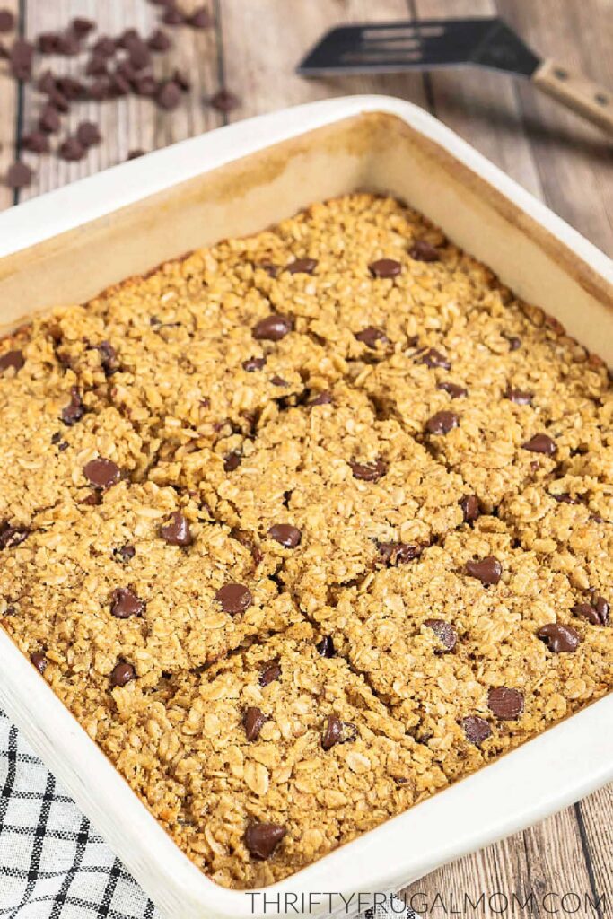 baked chocolate chip oatmeal cut into squares in a white baking dish next to striped towel