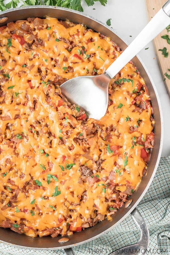 spanish rice with ground beef topped with cheese in a skillet with large silver spoon