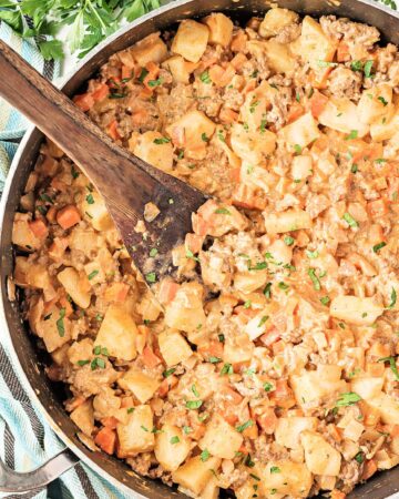 ground beef and potatoes in a large skillet with a wooden spoon next to a bunch of parsley
