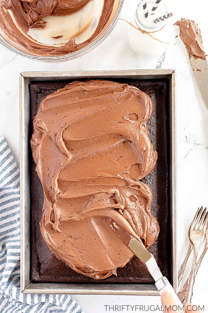 spreading easy buttercream frosting onto a chocolate cake in a pan with a spatula