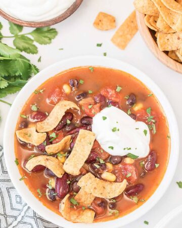 a bowl full of Mexican bean soup with sour cream and corn chips in a white bowl