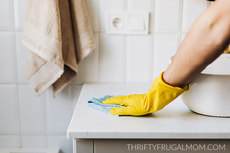 a yellow gloved hand wiping a bathroom countertop with a cloth rag