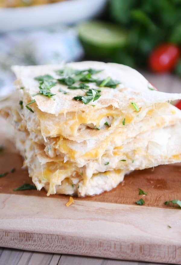 A stack of cheesy tuna quesadillas using flour tortillas on a wooden cutting board.