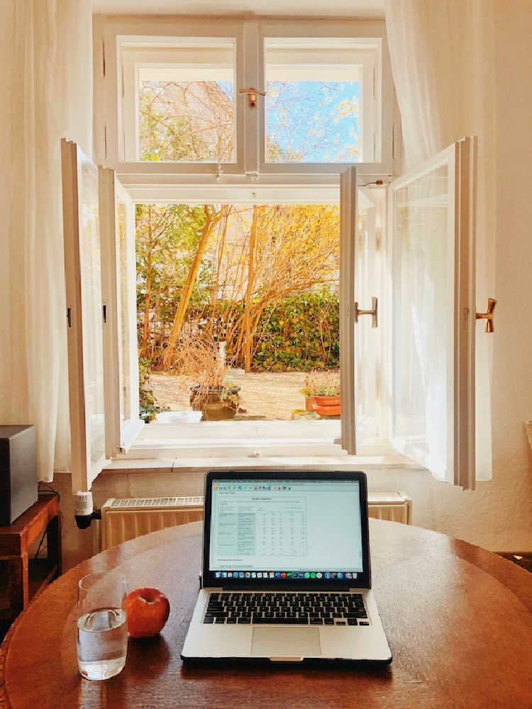 a table with a laptop, apple and drink sitting in front of an open window
