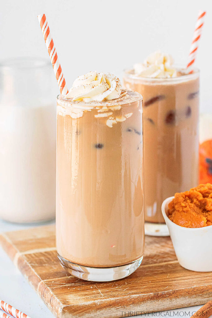 Two homemade pumpkin spice iced lattes next to each other with whipped cream and paper straws.