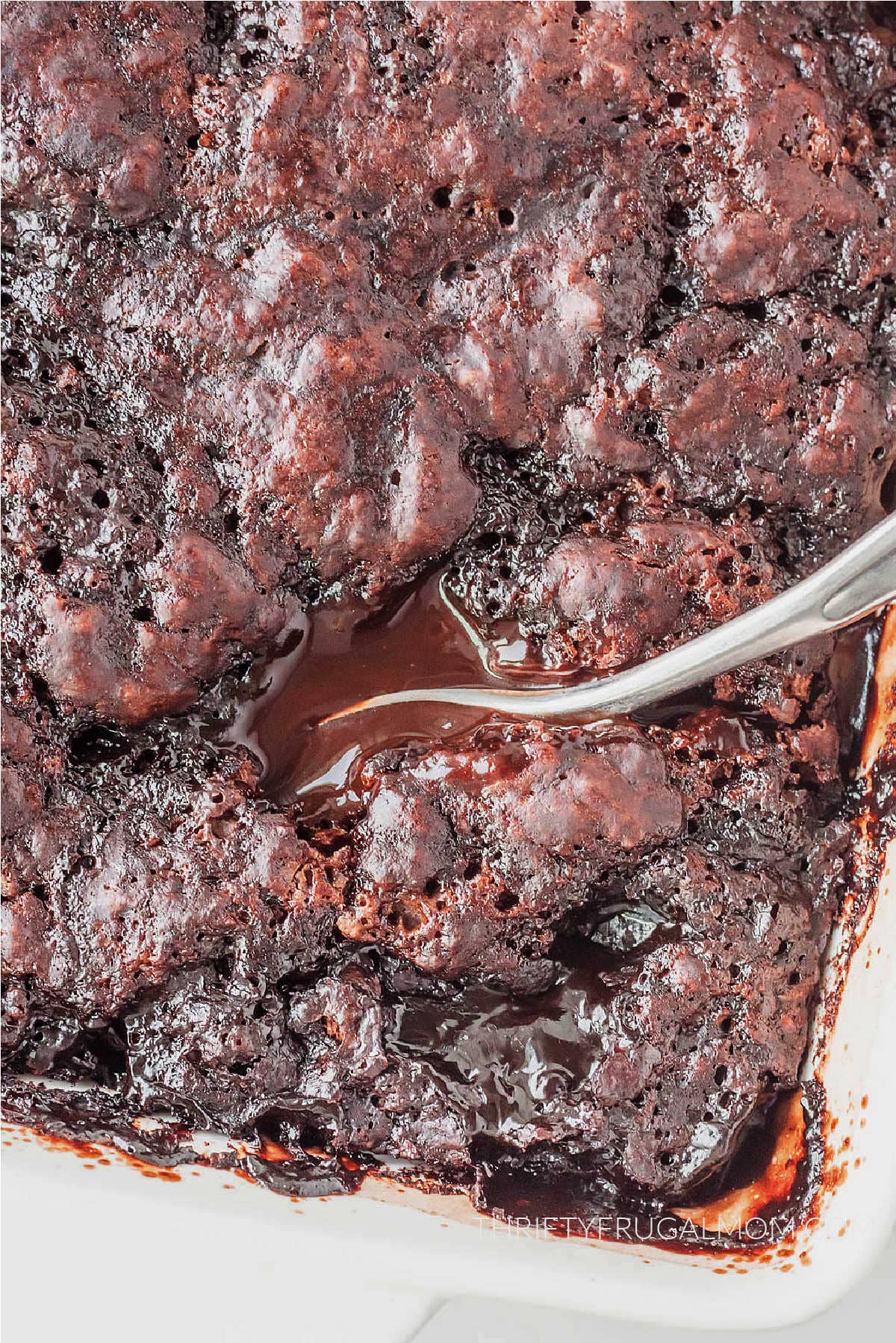 A large spoon stuck in the hot fudge chocolate cobbler.