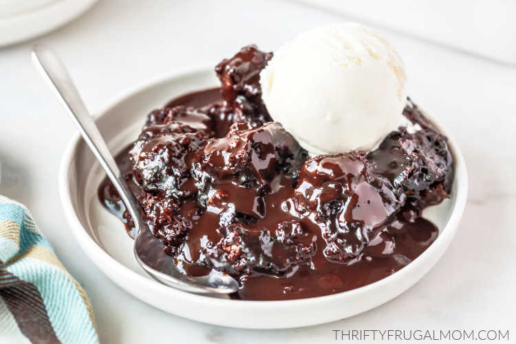 A scoop of chocolate cobbler with a spoon on a white plate topped with vanilla ice cream.